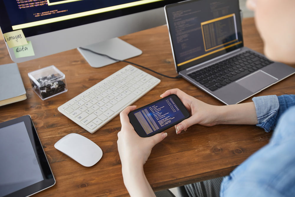 high-angle-closeup-female-hands-holding-smartphone-with-code-screen-while-working-desk-office-female-it-developer-concept-copy-space